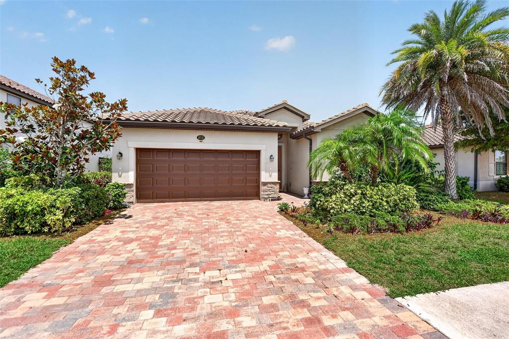 A single-story house features a brown garage door, a brick paver driveway, and palm trees — 20722 ROMAGNA PLACE, VENICE, FL