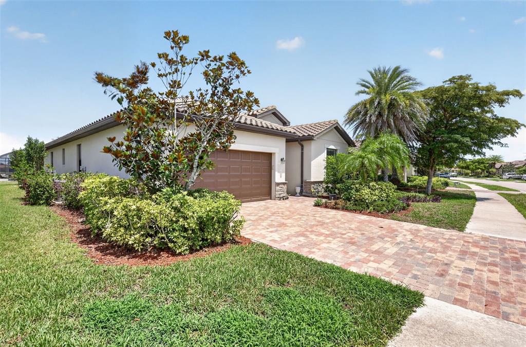 A single-story house with a brick paver driveway, a garage, and landscaping under a blue sky — 20722 ROMAGNA PLACE, VENICE, FL