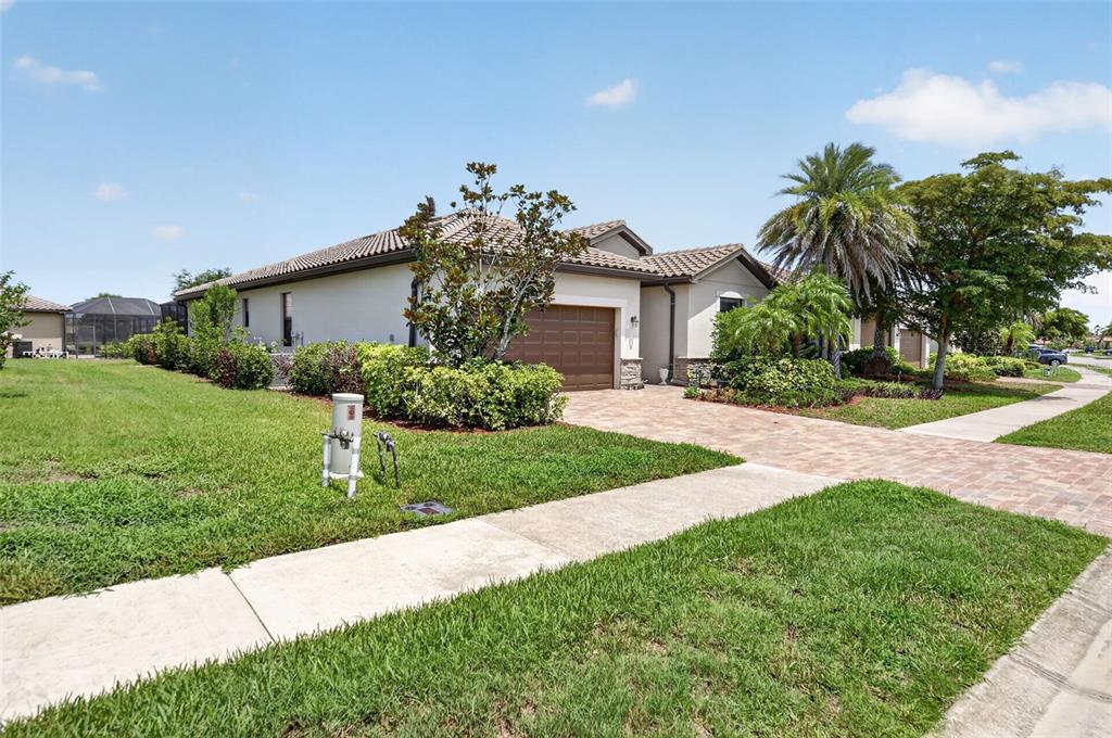 A single-story house with a brown garage, tile roof, and landscaped yard under a blue sky — 20722 ROMAGNA PLACE, VENICE, FL
