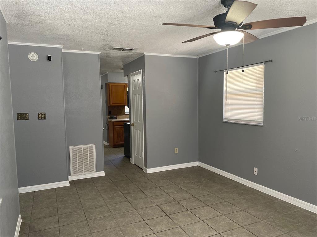 A room with gray walls, tile flooring, a ceiling fan, and a view into a kitchen — 1935 W 14TH STREET, SANFORD, FL