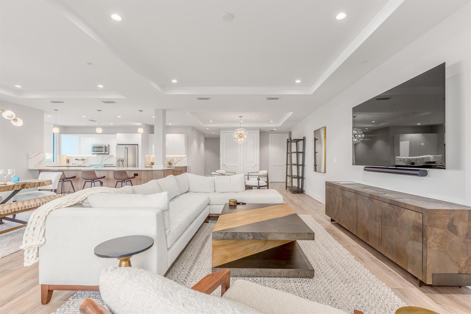 A bright open-concept living room features a white sectional sofa, wood coffee table, and television — 41 SW Seminole Street # 306, Stuart FL 34994, STUART, FL