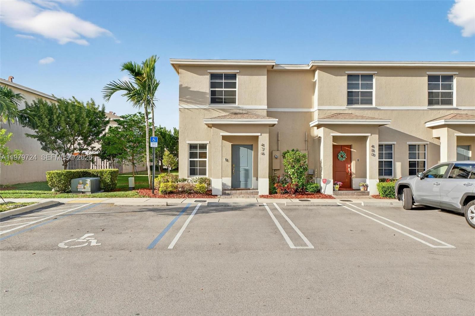 A two-story townhouse exterior features a gray front door, a parking space, and landscaping — 476 NE 4th Ln, Florida City FL 33034, FLORIDA CITY, FL