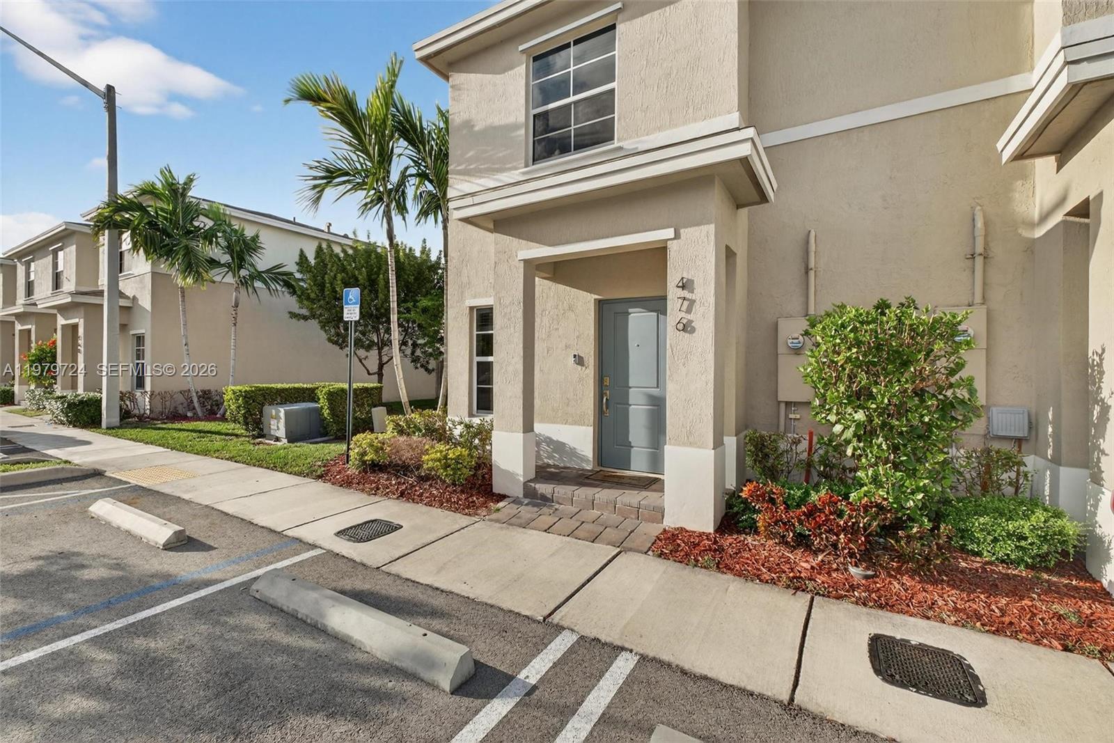 The exterior of a two-story beige townhouse features a gray front door and landscaping — 476 NE 4th Ln, Florida City FL 33034, FLORIDA CITY, FL