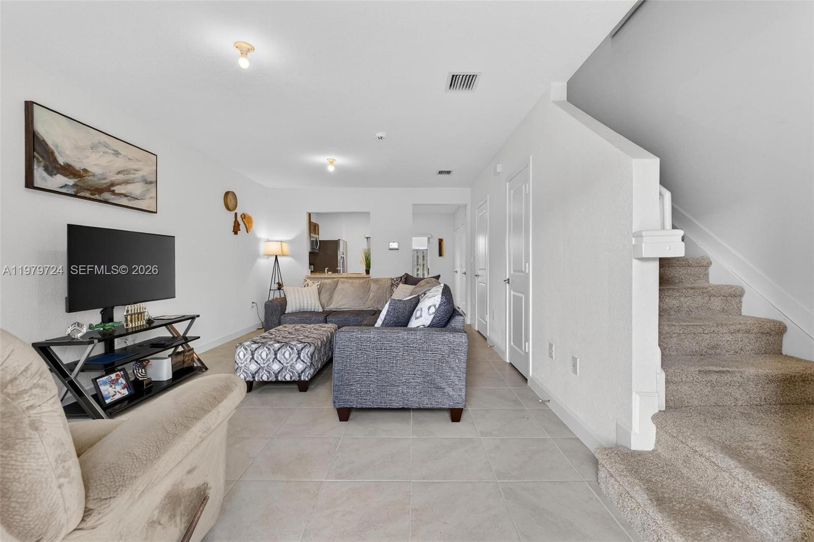 A living room features tile flooring, a sectional sofa, a television stand, and carpeted stairs — 476 NE 4th Ln, Florida City FL 33034, FLORIDA CITY, FL