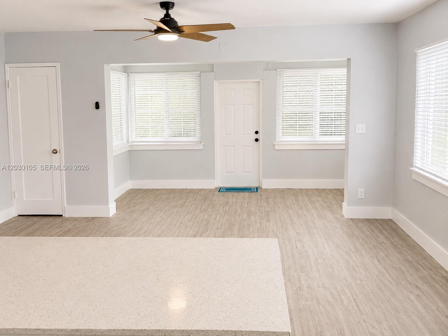 A bright room features light wood-look tile flooring, white walls, a ceiling fan, and windows — 209 SW 5th St # 209, Dania Beach FL 33004, DANIA BEACH, FL