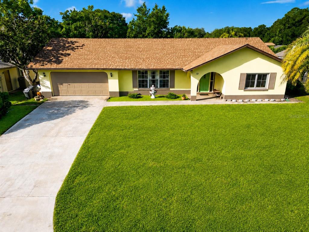 A single-story house with a yellow exterior, brown shingled roof, and a large front lawn — 10 BLACKBURN PLACE, PALM COAST, FL