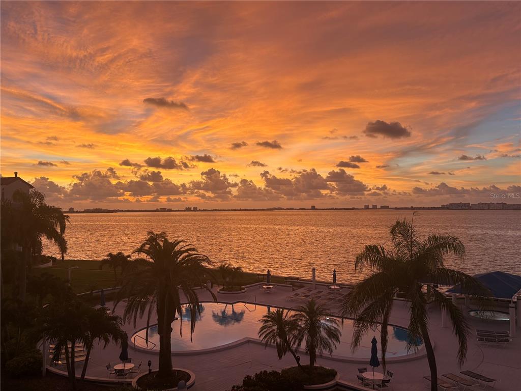 A swimming pool sits before a large body of water under a vibrant sunset sky — 5155 ISLA KEY BOULEVARD S UNIT 304, ST PETERSBURG, FL