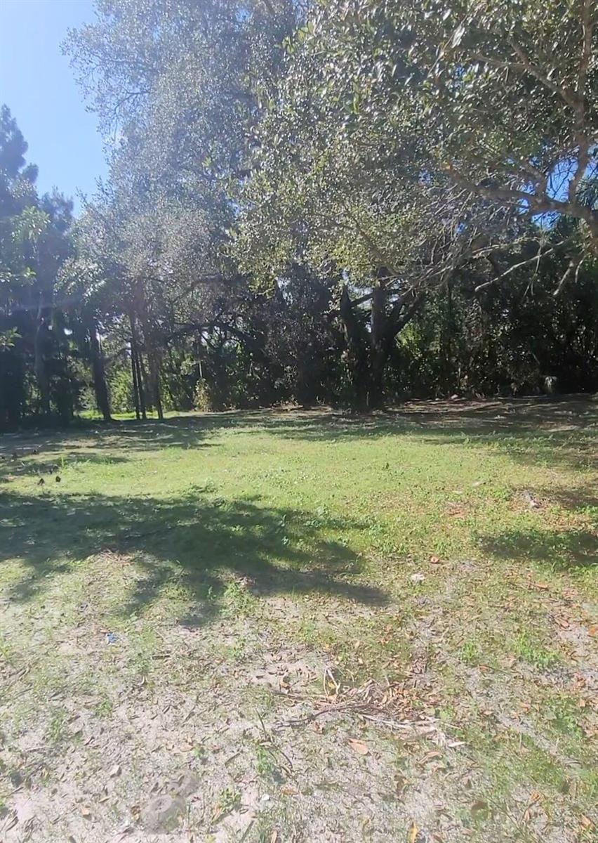 A grassy, partially shaded lot features several large trees and sandy patches of ground — 8511 64th Court, Vero Beach FL 32967, VERO BEACH, FL