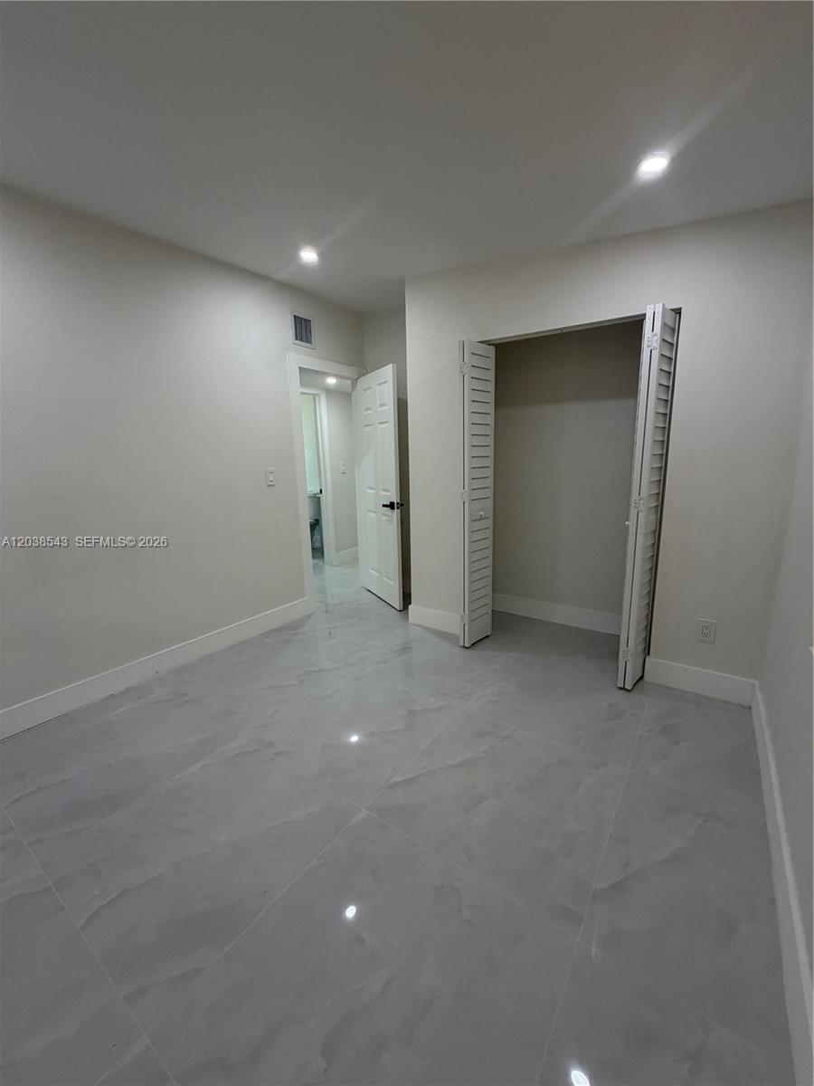 A room with light-colored walls, gray tile flooring, a closet, and an open doorway — OPA-LOCKA, FL