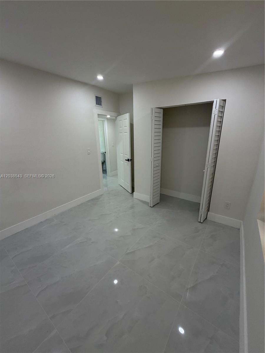 A room with light-colored walls, gray tile flooring, a closet, and an open doorway — OPA-LOCKA, FL