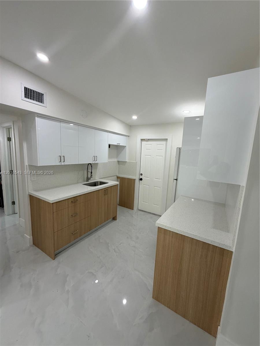 A modern kitchen features white upper cabinets, wood-toned lower cabinets, and white quartz countertops — OPA-LOCKA, FL