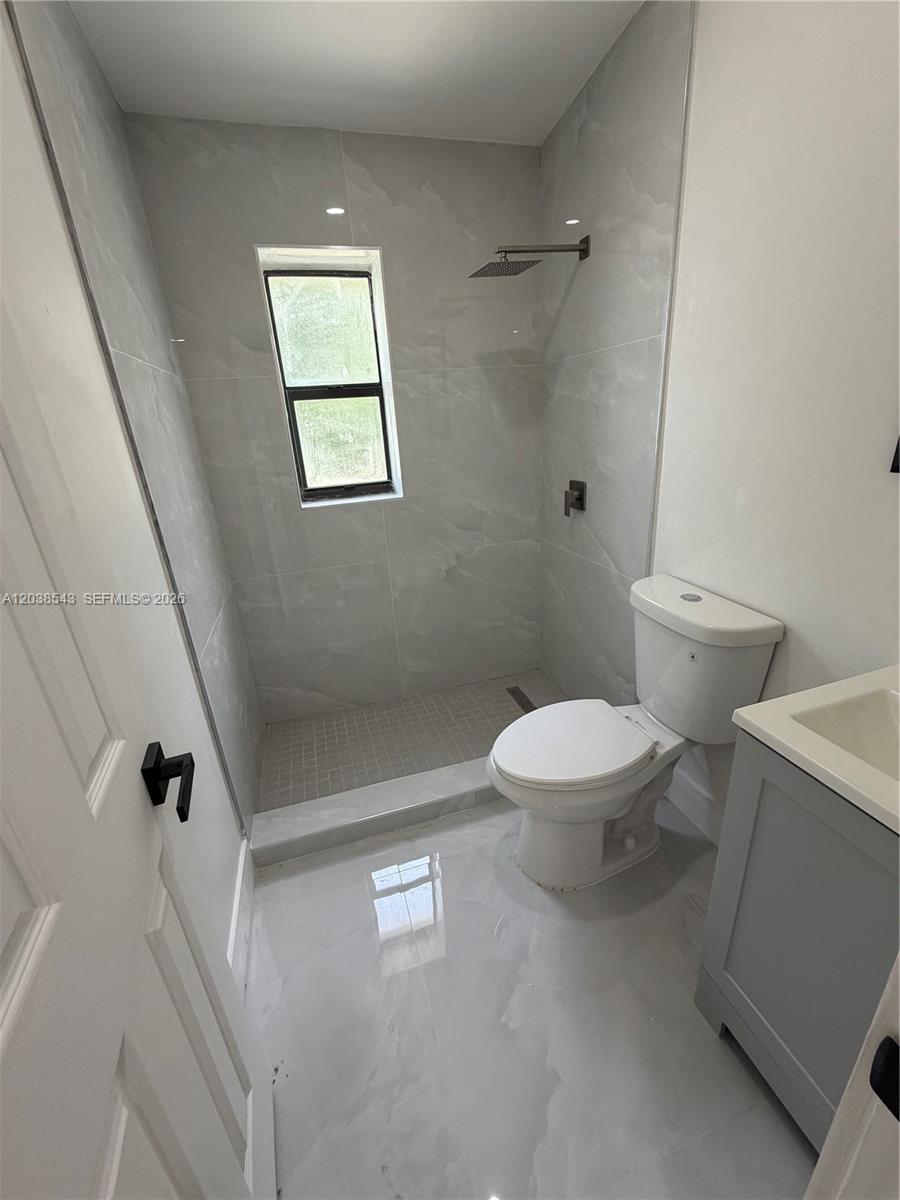 A small bathroom features a walk-in shower with gray tile and a white toilet — OPA-LOCKA, FL