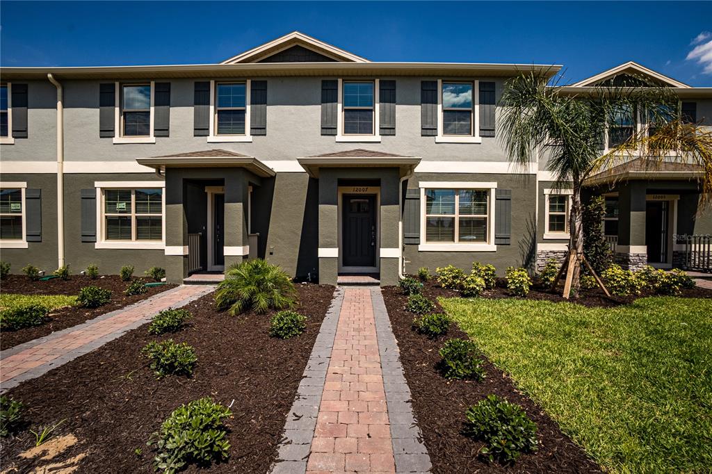 A multi-unit townhouse exterior features gray stucco walls, dark shutters, and paved walkways — 12007 HOLYSTONE STREET, WINTER GARDEN, FL