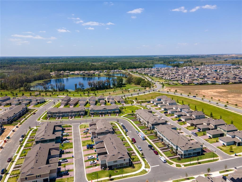 An aerial view shows a suburban neighborhood with townhomes, a lake, and surrounding green space — 12007 HOLYSTONE STREET, WINTER GARDEN, FL