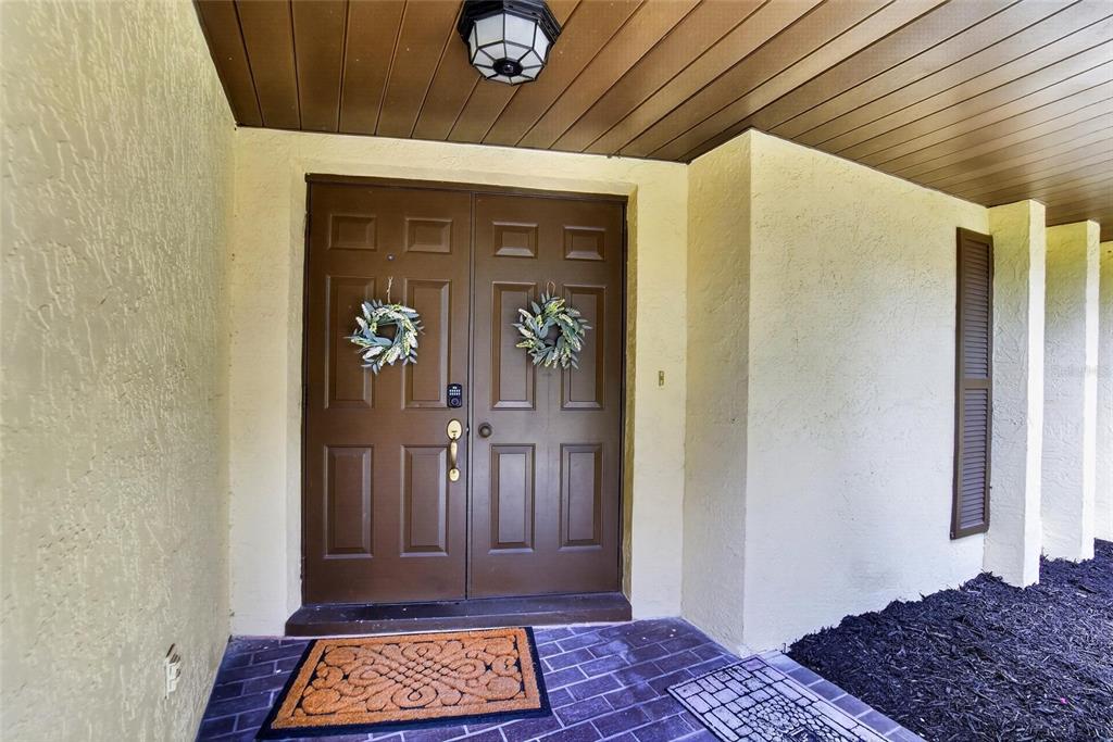 A brown double front door with wreaths sits under a covered porch with brick flooring — 3708 JOE SANCHEZ RD, PLANT CITY, FL