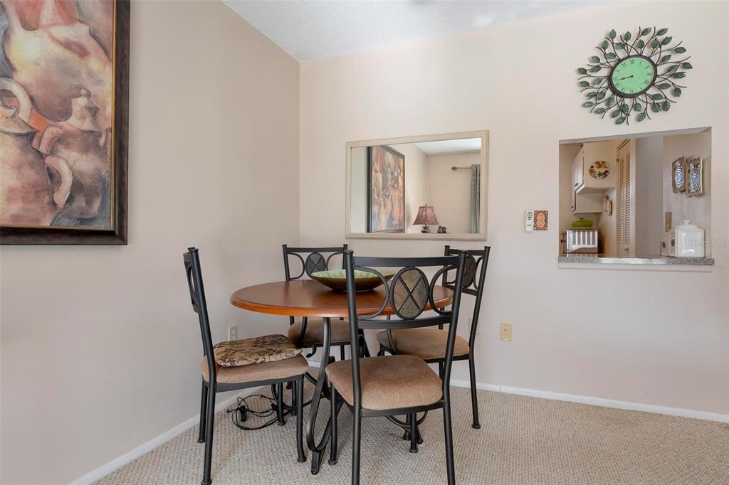 A dining area features a round wooden table with four chairs, a mirror, and wall art — 4040 IRONWOOD CIRCLE UNIT 102F, BRADENTON, FL