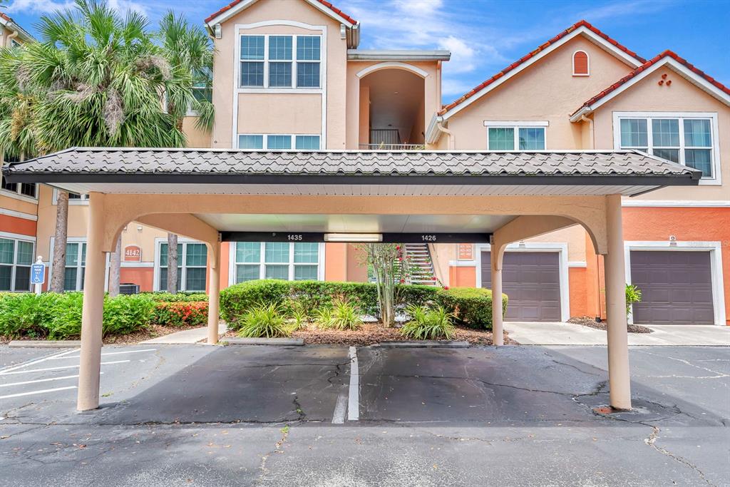 A covered parking structure sits in front of a multi-story residential building with stucco walls — 4142 CENTRAL SARASOTA PARKWAY UNIT 1426, SARASOTA, FL