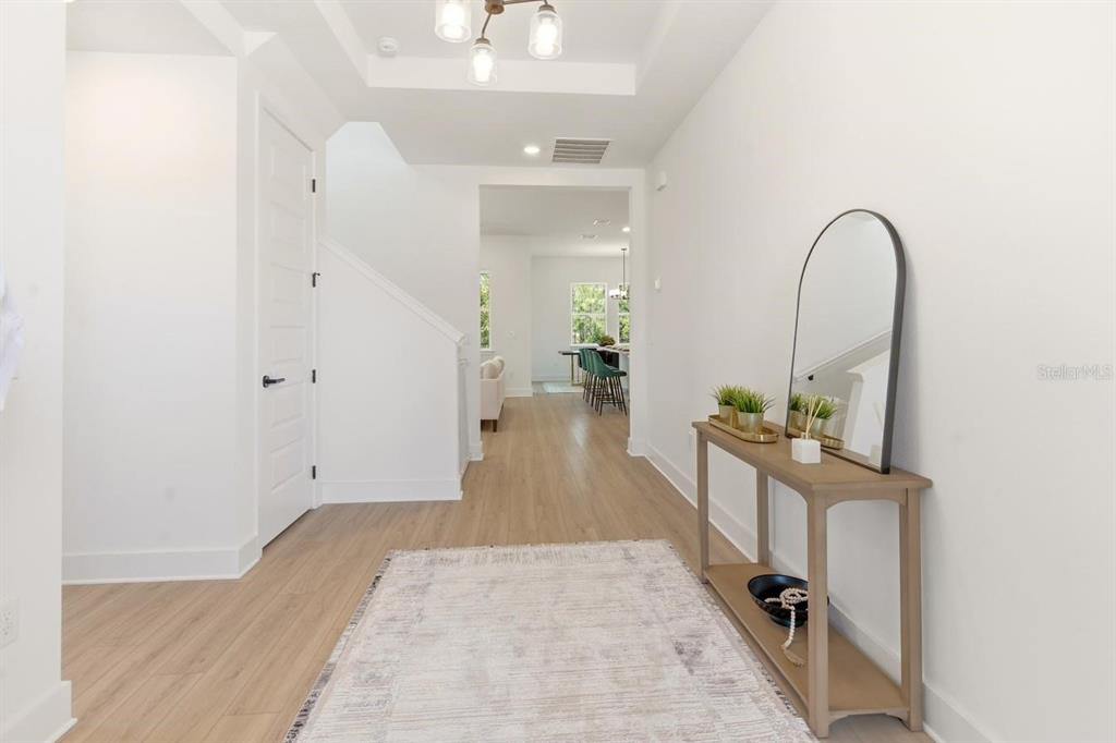 A bright entryway features light wood flooring, a console table with a mirror, and stairs — 13086 SUNRISE HARVEST DRIVE, WINTER GARDEN, FL