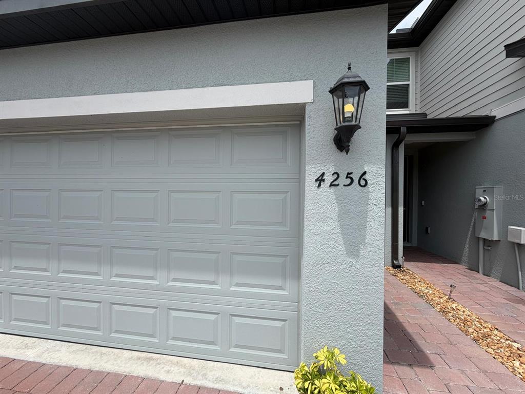 A gray garage door sits next to a brick walkway and a wall-mounted outdoor light — 4256 RANCH HOUSE ROAD, ST CLOUD, FL