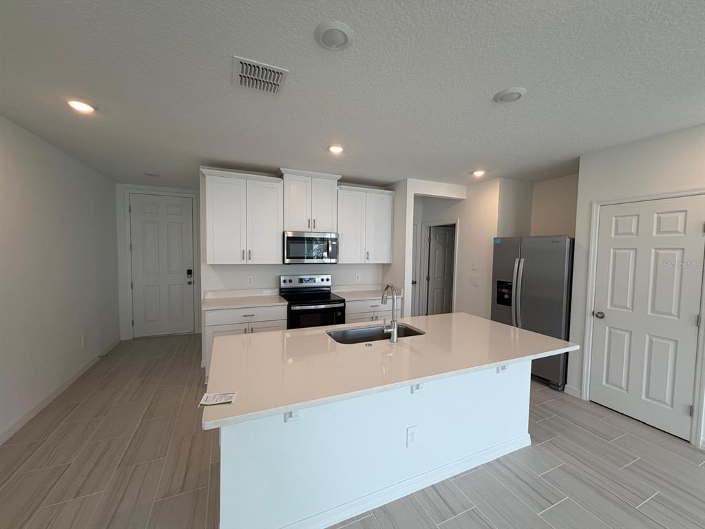 A kitchen features white cabinets, stainless steel appliances, a quartz island, and light tile flooring — 4256 RANCH HOUSE ROAD, ST CLOUD, FL