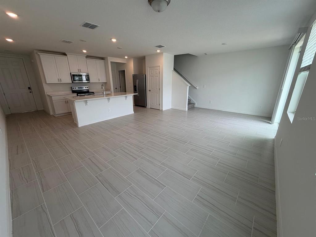 An open-concept kitchen and living area feature white cabinetry, stainless appliances, and light tile flooring — 4256 RANCH HOUSE ROAD, ST CLOUD, FL