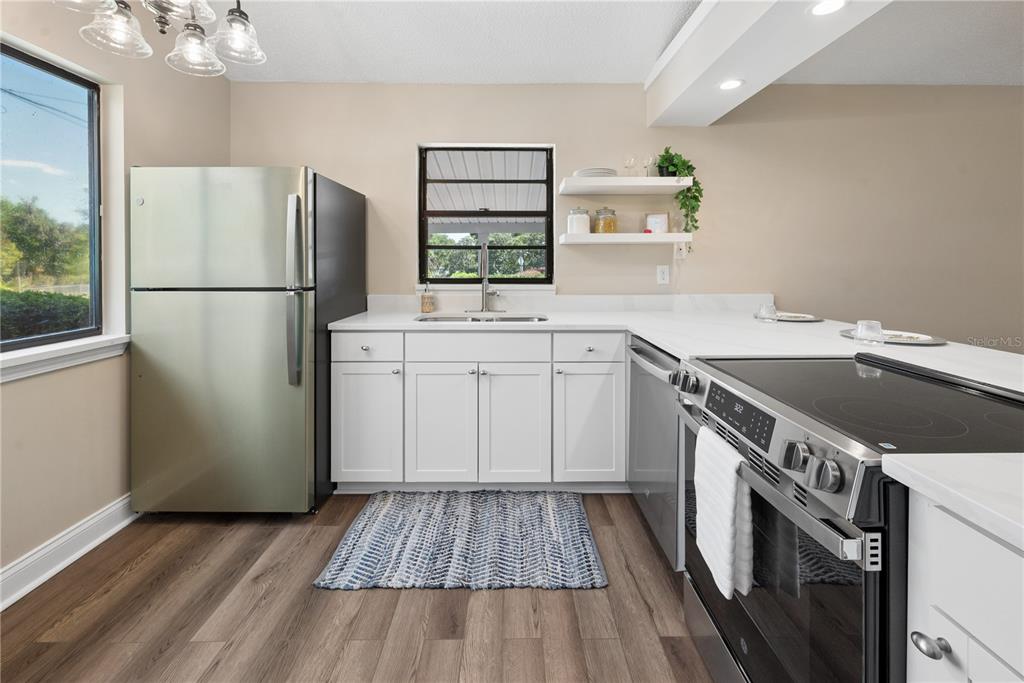 A kitchen features white cabinets, stainless steel appliances, wood-look flooring, and a window above the sink — 950 S LAWRENCE BOULEVARD, KEYSTONE HEIGHTS, FL