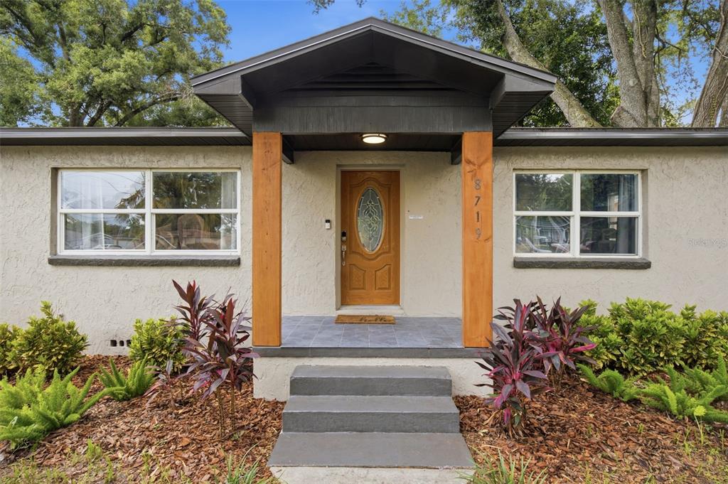 The exterior of a house features a covered entryway with wood pillars and a front door — 8719 N TEMPLE AVENUE, TAMPA, FL