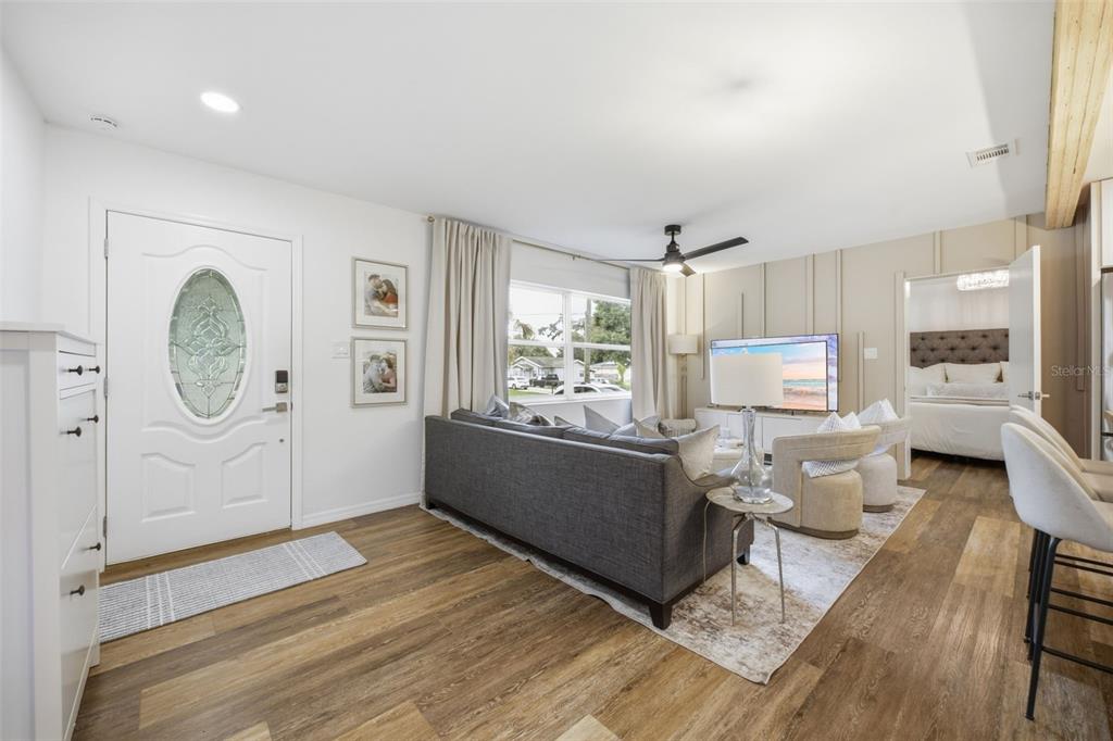 A living room features wood-look flooring, a gray sofa, a television, and an entryway door — 8719 N TEMPLE AVENUE, TAMPA, FL