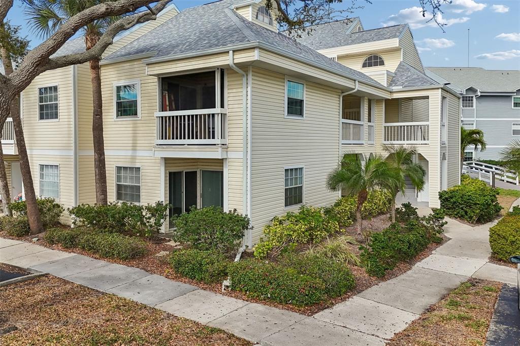 A two-story yellow building with a screened balcony and surrounding landscaping — 6915 STONES THROW CIRCLE N UNIT 3106, ST PETERSBURG, FL