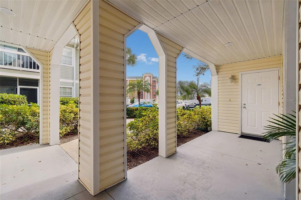 A covered concrete porch features beige siding, arched support columns, and a white entry door — 6915 STONES THROW CIRCLE N UNIT 3106, ST PETERSBURG, FL