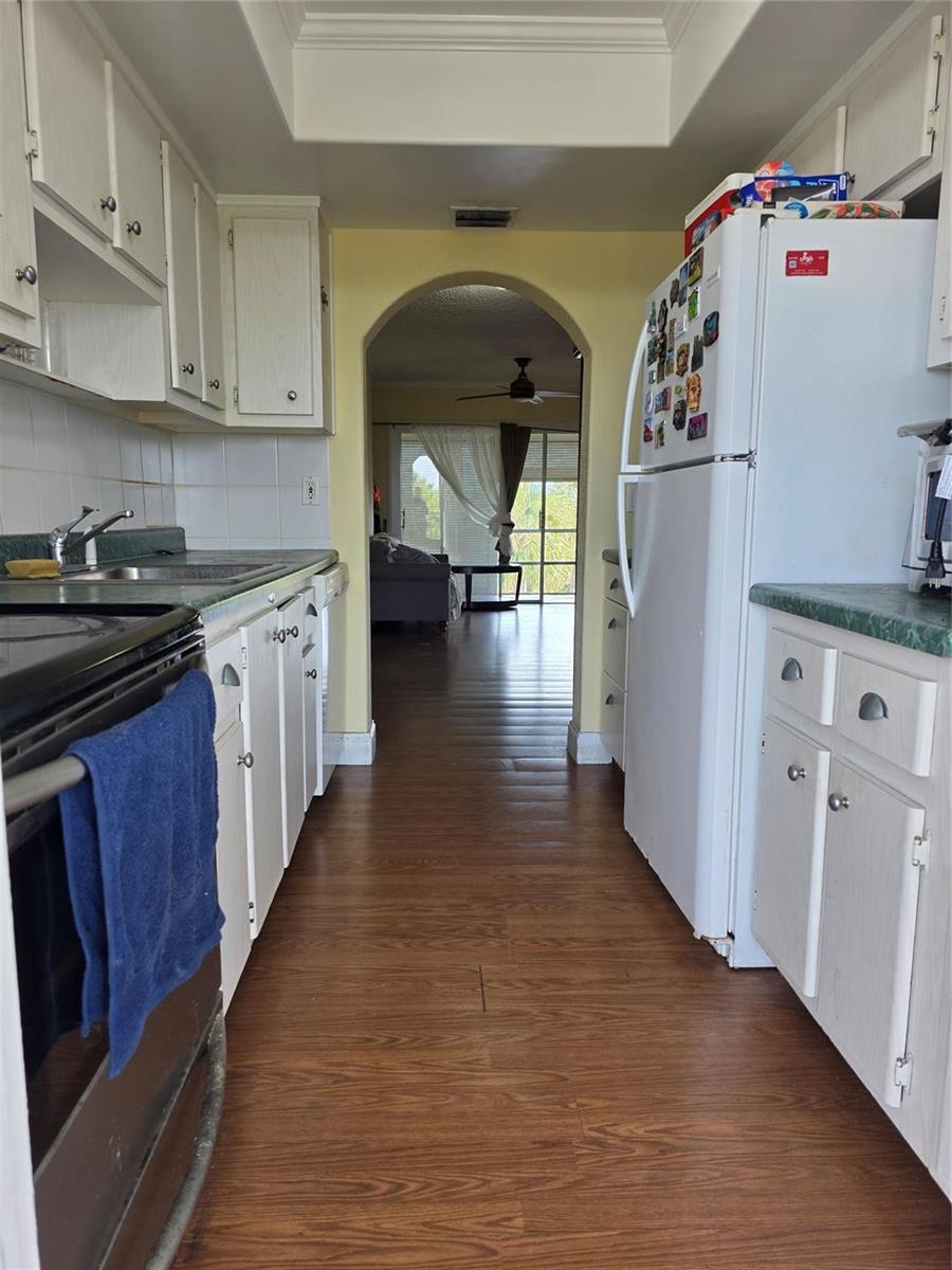 A galley kitchen with white cabinets, green countertops, and wood-look flooring leads to an arched doorway — 5800 Margate Boulevard # 347, Pompano Beach FL 33063, POMPANO BEACH, FL