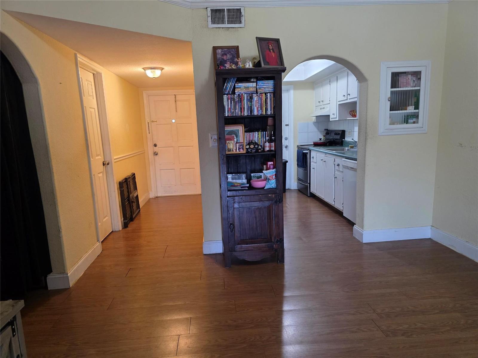 A wooden bookshelf stands between a hallway leading to an entryway and an arched kitchen — 5800 Margate Boulevard # 347, Pompano Beach FL 33063, POMPANO BEACH, FL