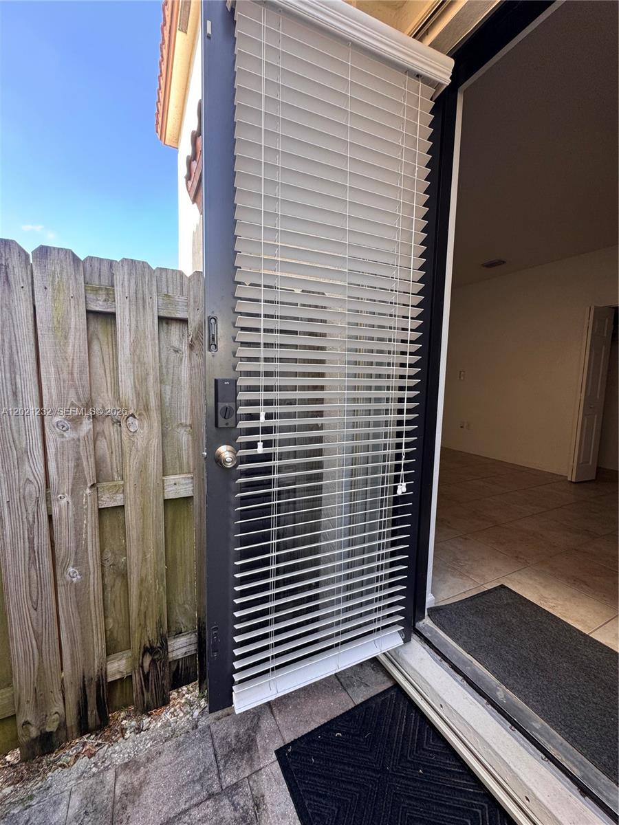 A door with white horizontal blinds opens from a tiled room to a wooden fence — 15400 SW 173rd St # 2, Miami FL 33187, MIAMI, FL