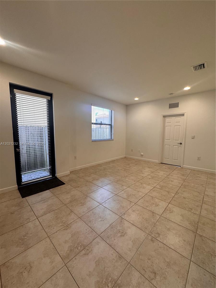 An empty room features light-colored tile flooring, white walls, a glass door, and a window — 15400 SW 173rd St # 2, Miami FL 33187, MIAMI, FL