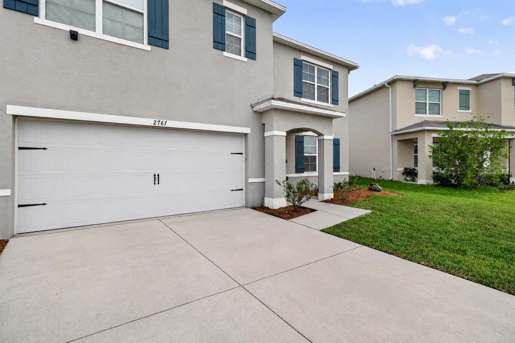 A two-story suburban house with a gray stucco exterior, blue shutters, and a concrete driveway — 2767 GRANDBURY GROVE ROAD, LAKELAND, FL