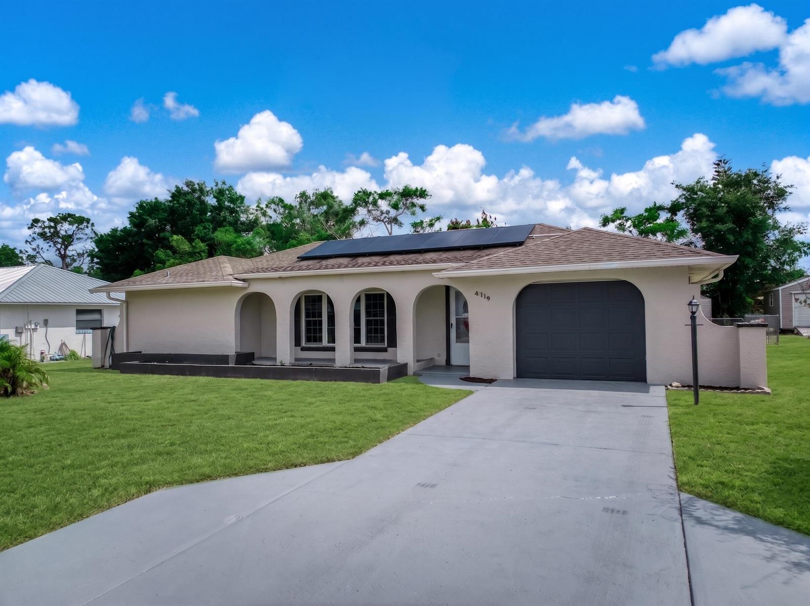 A single-story house with a gray garage door, arched entryway, and solar panels on the roof — 4119 Tangier Street, Sebring FL 33872, SEBRING, FL