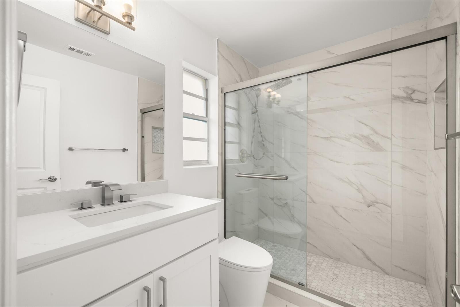 A modern bathroom features a white vanity, marble-look wall tiles, and a glass-enclosed walk-in shower — 4119 Tangier Street, Sebring FL 33872, SEBRING, FL