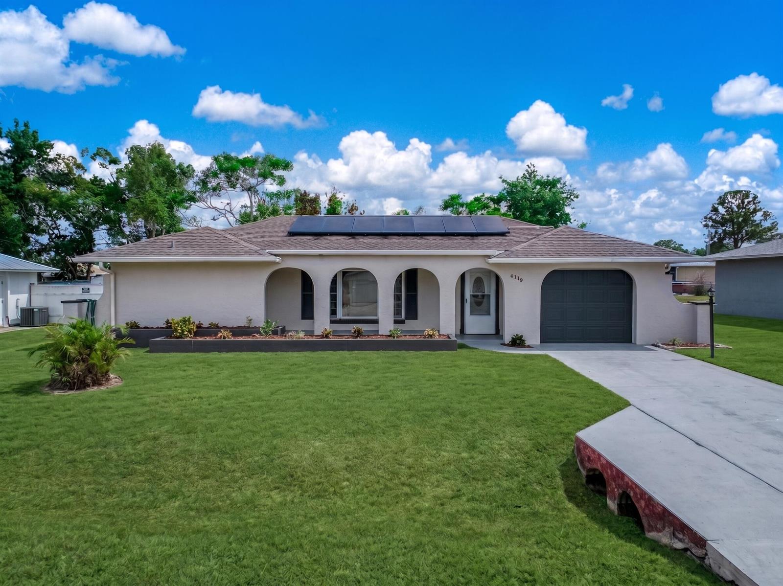 A single-story house with a tan stucco exterior, arched porch, solar panels, and a driveway — 4119 Tangier Street, Sebring FL 33872, SEBRING, FL