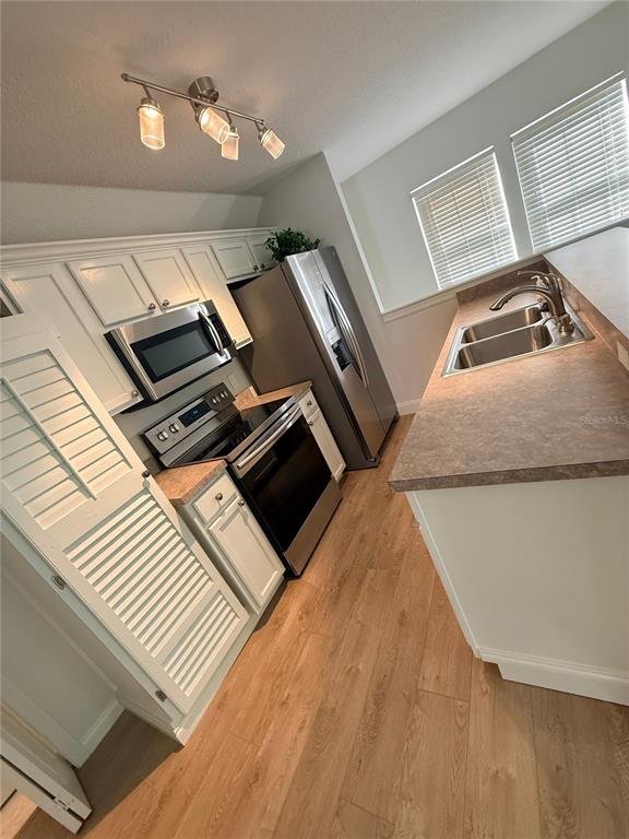 A kitchen features white cabinets, stainless steel appliances, a double sink, and wood-look flooring — 1005 KESTREL COURT UNIT B, CELEBRATION, FL
