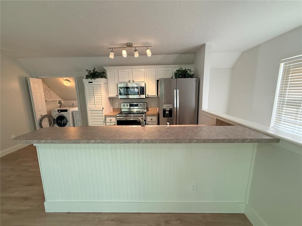 A kitchen with a breakfast bar, white cabinets, stainless steel appliances, and an adjacent laundry area — 1005 KESTREL COURT UNIT B, CELEBRATION, FL