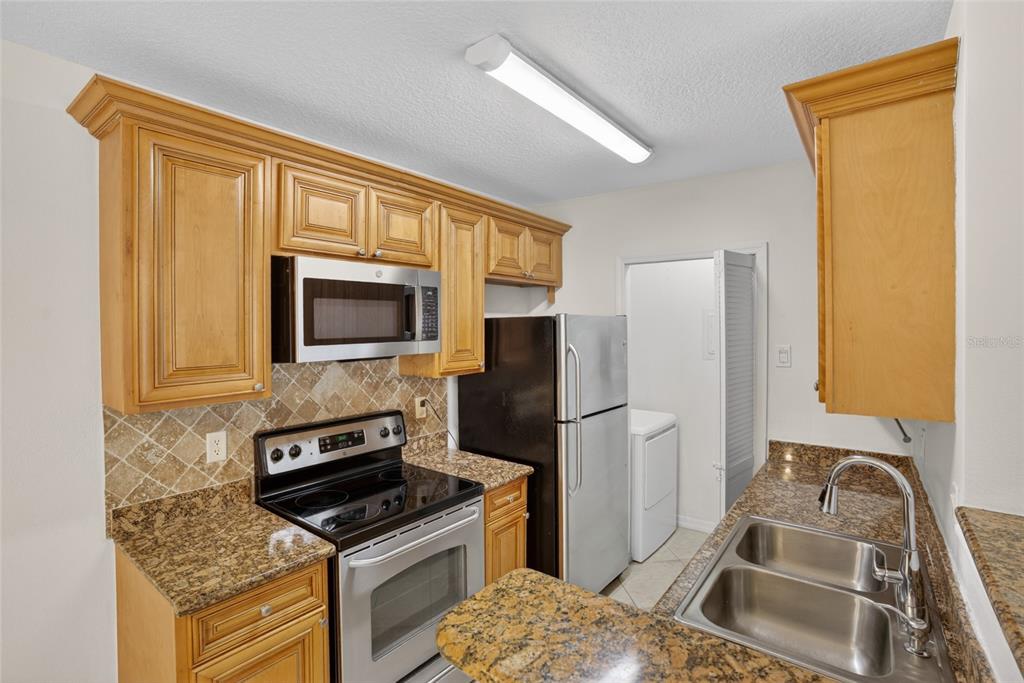 A kitchen features wood cabinets, granite countertops, stainless steel appliances, and a double sink — 4364 S KIRKMAN ROAD UNIT 307, ORLANDO, FL