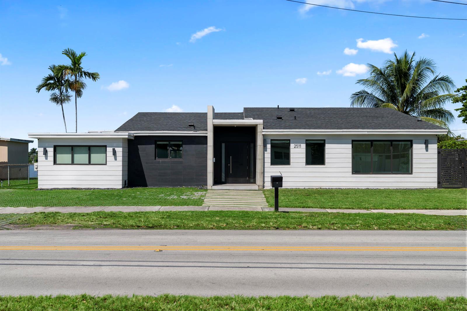 A modern single-story house features a black and white exterior with a central entryway — 2511 NE 209th Terrace, Miami FL 33180, MIAMI, FL