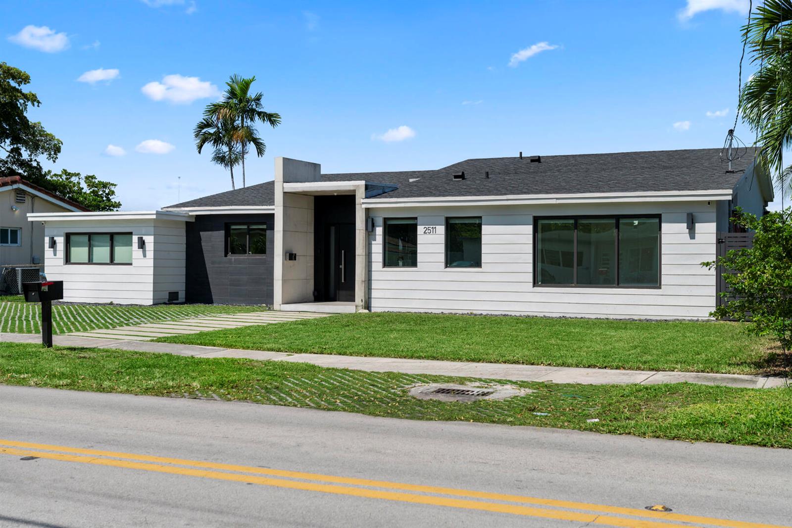 A modern single-story house with white horizontal siding, a dark roof, and a concrete entryway — 2511 NE 209th Terrace, Miami FL 33180, MIAMI, FL