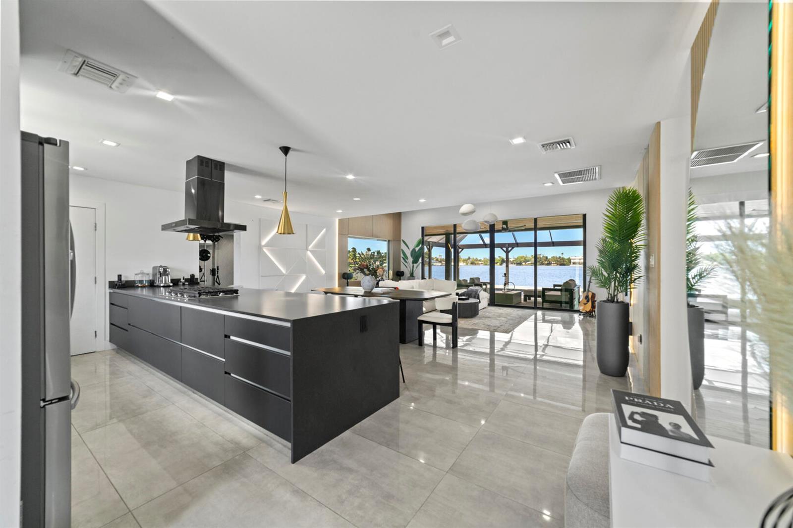 A modern open-concept kitchen and living area with a large dark island overlooking a lake — 2511 NE 209th Terrace, Miami FL 33180, MIAMI, FL