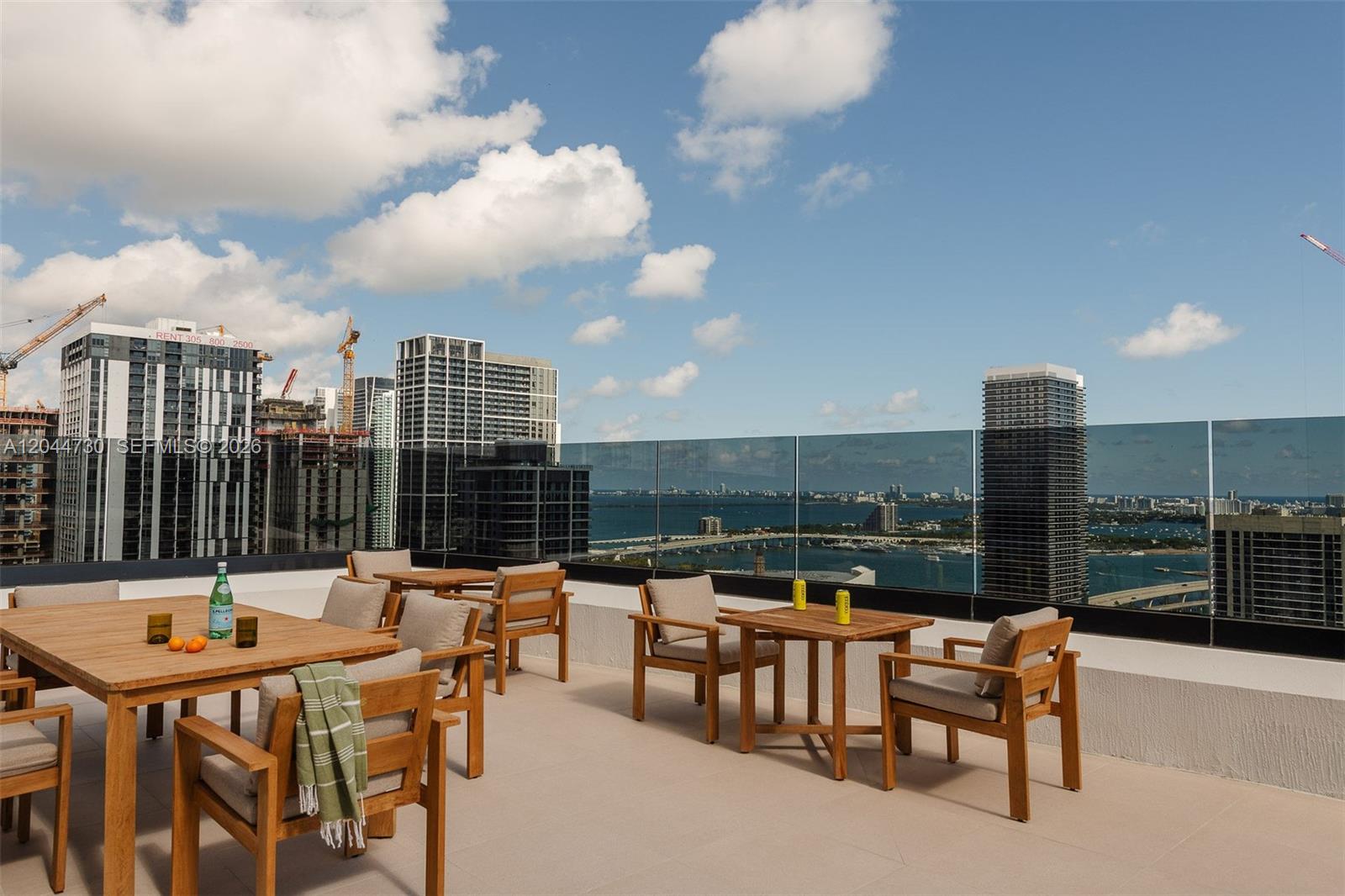 An outdoor rooftop terrace features wooden dining sets overlooking a city skyline and bay — 225 N Miami Ave # 3412, Miami FL 33128, MIAMI, FL