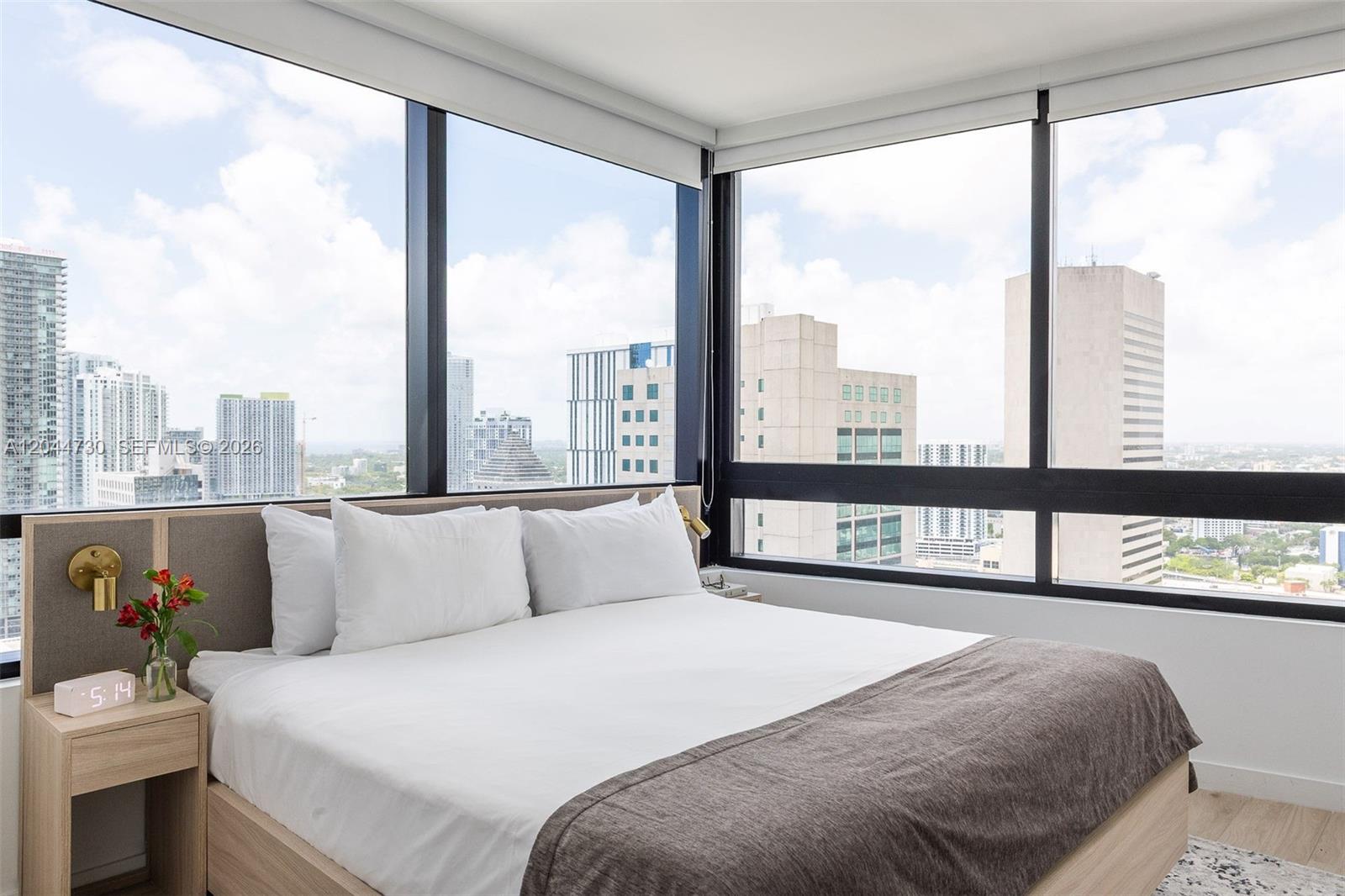 A bedroom features a bed against a corner window with expansive city skyline views — 225 N Miami Ave # 3412, Miami FL 33128, MIAMI, FL