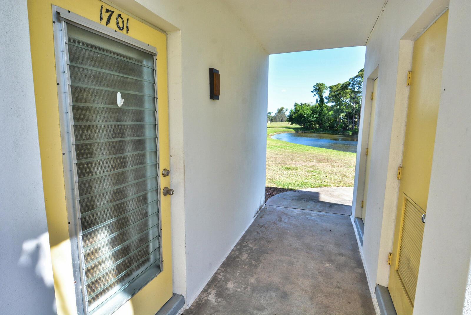 A concrete walkway leads to two yellow doors with a view of a pond outside — 1225 NW 21st Street # 1701, Stuart FL 34994, STUART, FL