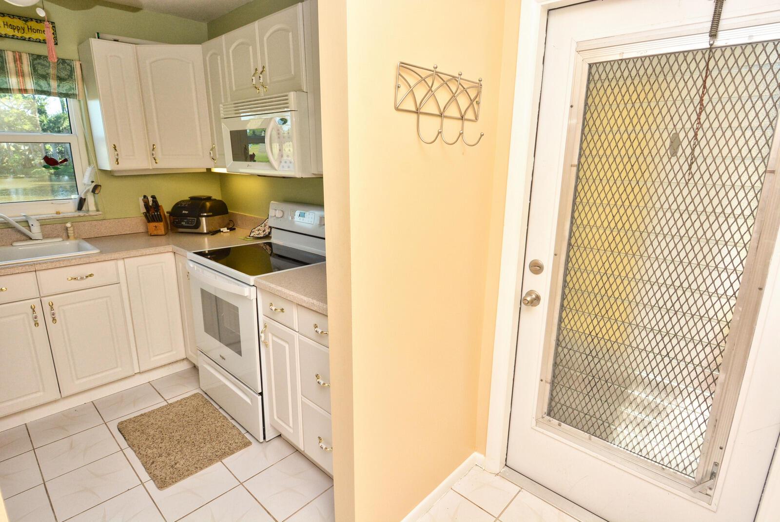 A kitchen with white cabinets, light countertops, and a white door with a metal screen — 1225 NW 21st Street # 1701, Stuart FL 34994, STUART, FL