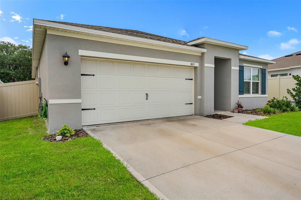 A single-story house exterior features a two-car garage, a concrete driveway, and blue window shutters — 1421 CUMBERLAND AVENUE, DAVENPORT, FL