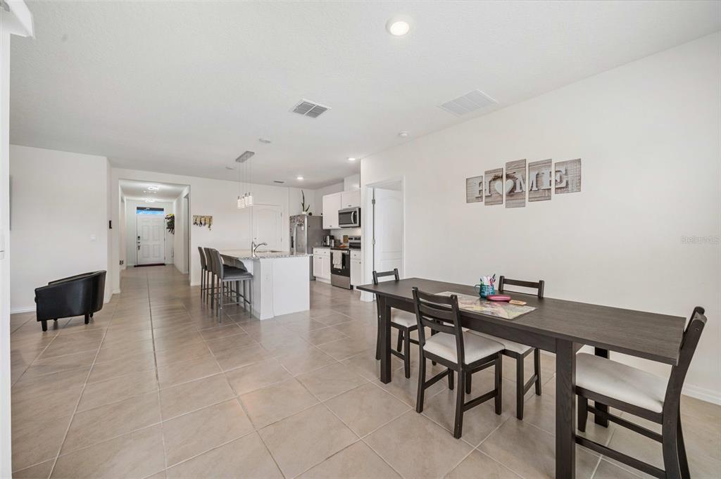 An open-concept kitchen and dining area features tile flooring, white cabinetry, and dark wood furniture — 1421 CUMBERLAND AVENUE, DAVENPORT, FL